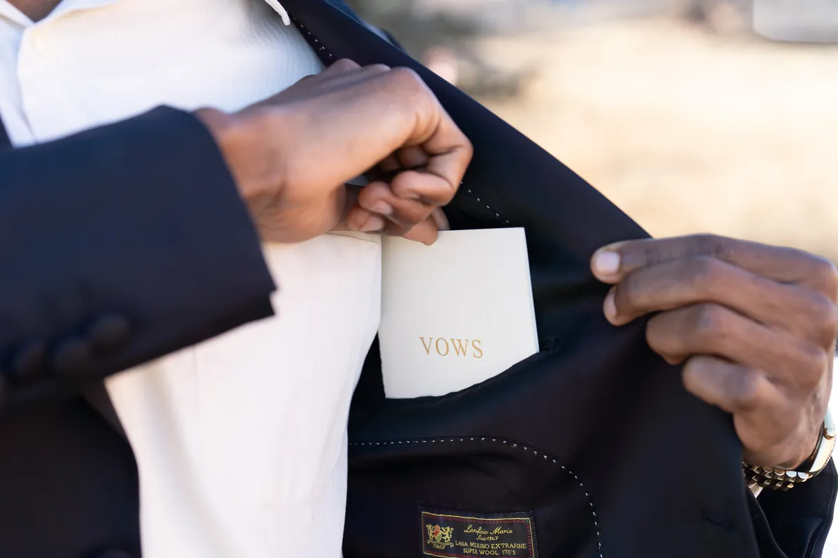 A groom tucking his gold-foil Vows book into his suit jacket.